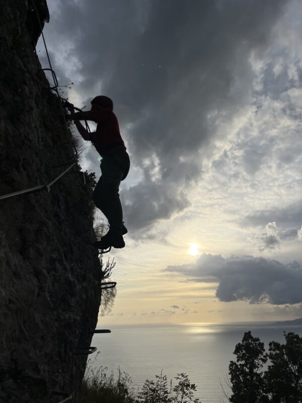 ferrata del cristo redentore di maratea: ragazzo in controluce che scala con il mare sullo sfondo