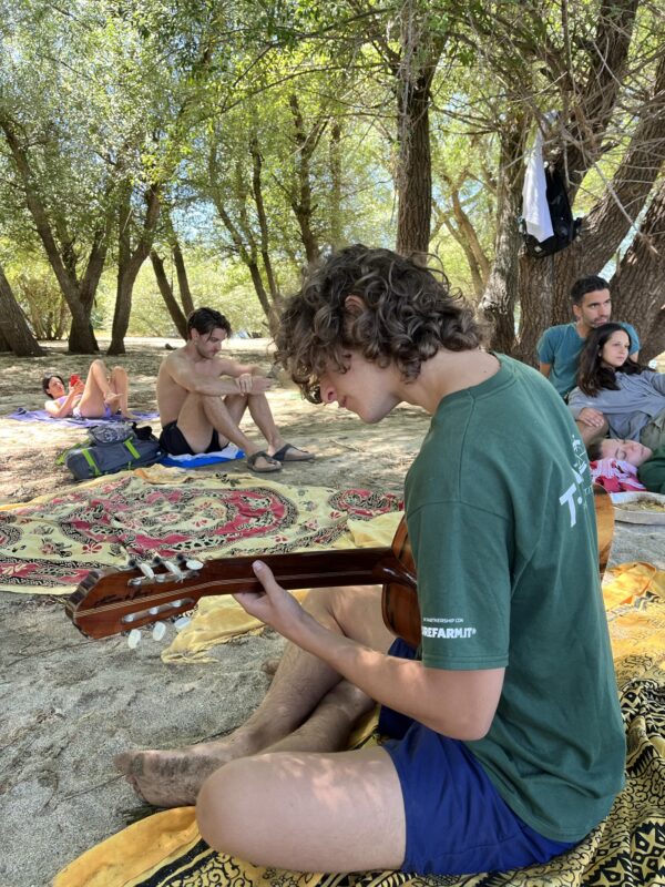 evento in Calabria dal nome emotional village a cura di Tspace: musicista suona a lago la chitarra mentre gli altri si rilassano sulla spiaggia